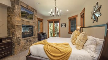 A bedroom with a stone fireplace, a large bed with a yellow throw blanket, and a chandelier.