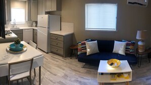 A compact living space with a kitchenette, a sofa, a small table, and a window with blinds. - ALL INCLUSIVE AMENITIES:Kayak,SUP,Pedal Boat,PingPong,Pickleball,Movie Nt &MORE! (Nice)