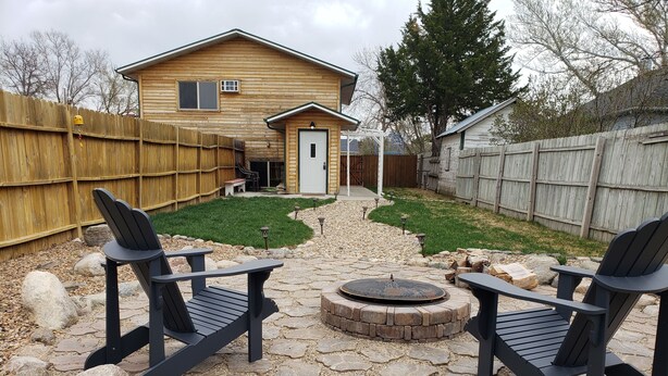 Un cortile con un patio in pietra, due poltrone Adirondack, un braciere e una casa in legno.