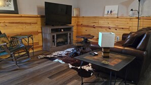 Un accogliente soggiorno con parete in legno, divano in pelle, poltrona a dondolo, televisore a schermo piatto e tavolino da caffè.