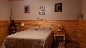 A cozy room with a wooden headboard, a bed with a beige comforter, two bedside tables with lamps, and three wall-mounted artworks.