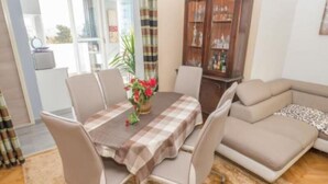 A dining area with a table set for four, surrounded by chairs. There is a sofa and a cabinet with bottles in the background. - Kike Apartments (Split)