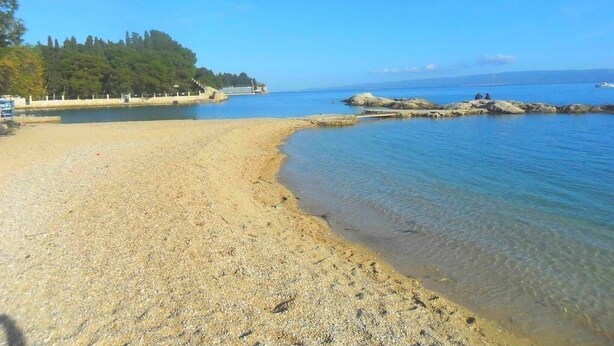 A beach with clear water, pebbly shore, and a forested area in the background. - Kike Apartments (Split)