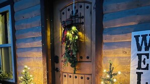 A wooden cabin with a door adorned with a wreath and lights, a 'WELCOME' sign, and two lit Christmas trees. - Romantic Cabin in Broken Bow! Secluded on 4+ acres, 1BR 2Bath, Hot Tub, FirePit (Broken Bow)