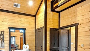 A wooden-paneled bedroom with a large bed, two doors, and a view into another room. - Romantic Cabin in Broken Bow! Secluded on 4+ acres, 1BR 2Bath, Hot Tub, FirePit (Broken Bow)