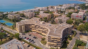A multi-story hotel with a curved facade, parking lot, and a view of the sea. - Résidence Partenaire Héliotel Marine (Saint-Laurent-du-Var)