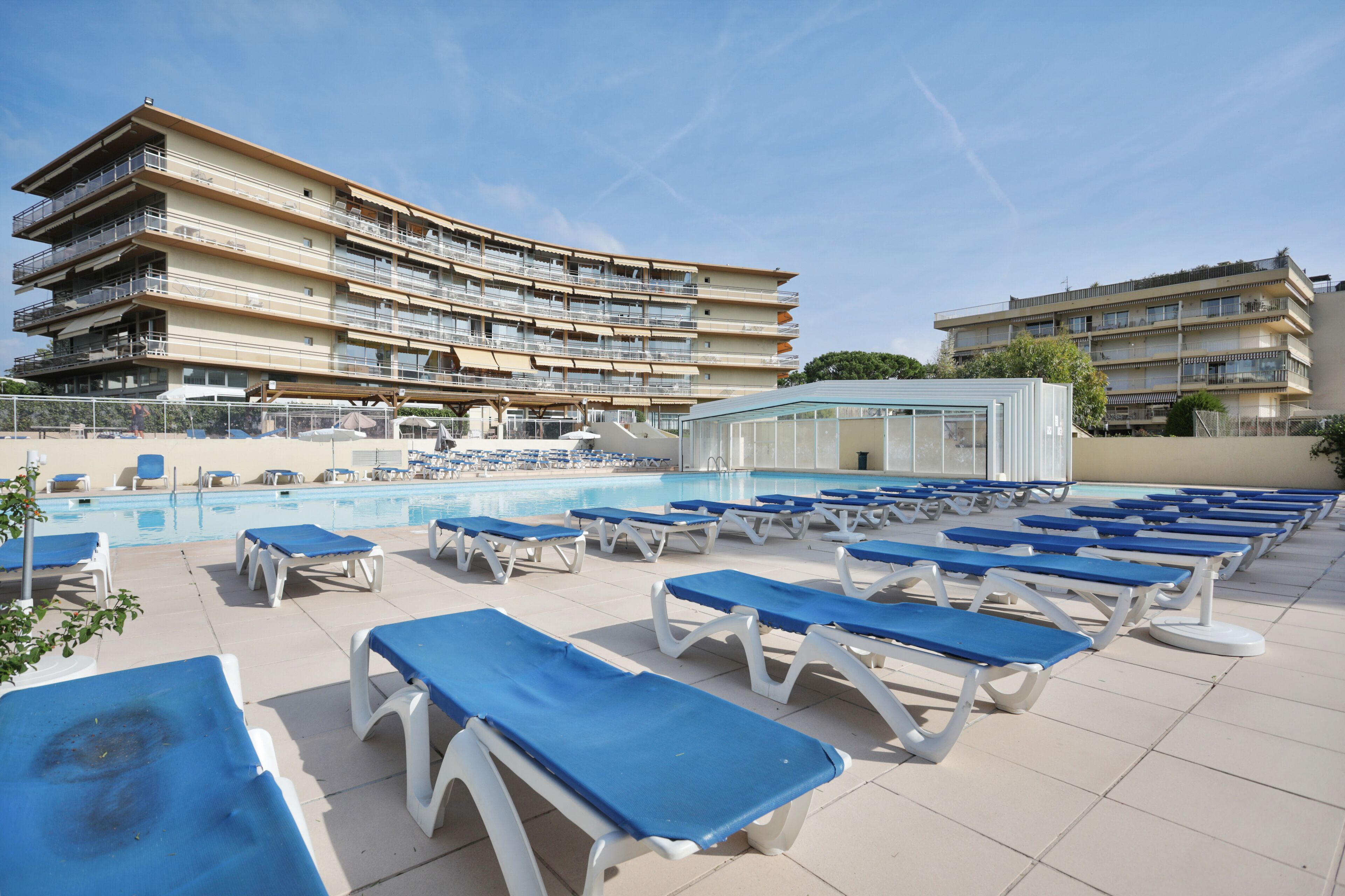 A poolside area with sun loungers and a large building with multiple balconies.
