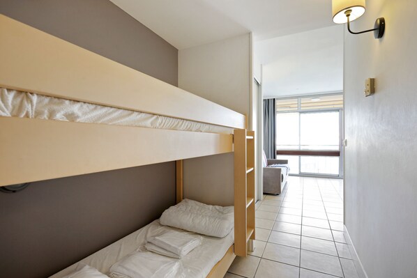 A bunk bed room with a window and a door leading to another room.