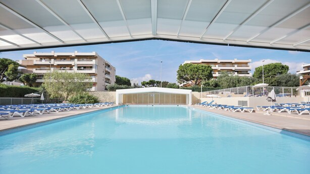 A swimming pool with blue lounge chairs and a covered area. - Résidence Partenaire Héliotel Marine (Saint-Laurent-du-Var)