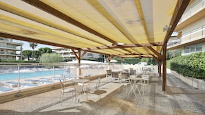 A covered outdoor area with a pool, lounge chairs, and tables. - Résidence Partenaire Héliotel Marine (Saint-Laurent-du-Var)