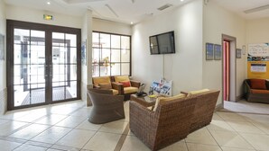 A reception area with wicker furniture, a flat-screen TV, and informational posters on the walls. - Résidence Partenaire Héliotel Marine (Saint-Laurent-du-Var)