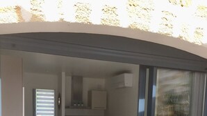 A compact living space with a sliding glass door leading to a balcony, a small kitchenette, a sofa, and a wicker chair. - Chez Simone ( 6 pers.) (Ensuès-la-Redonne)