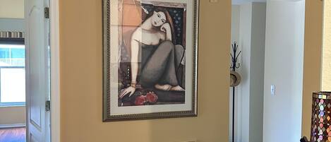 A hallway with beige walls, a framed artwork, a vent, and a door leading to another room.