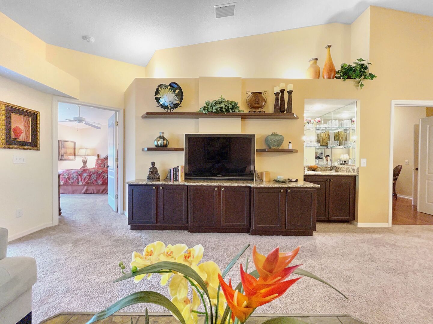 A living room with a TV, dark cabinets, a plant, and a vase on a shelf.