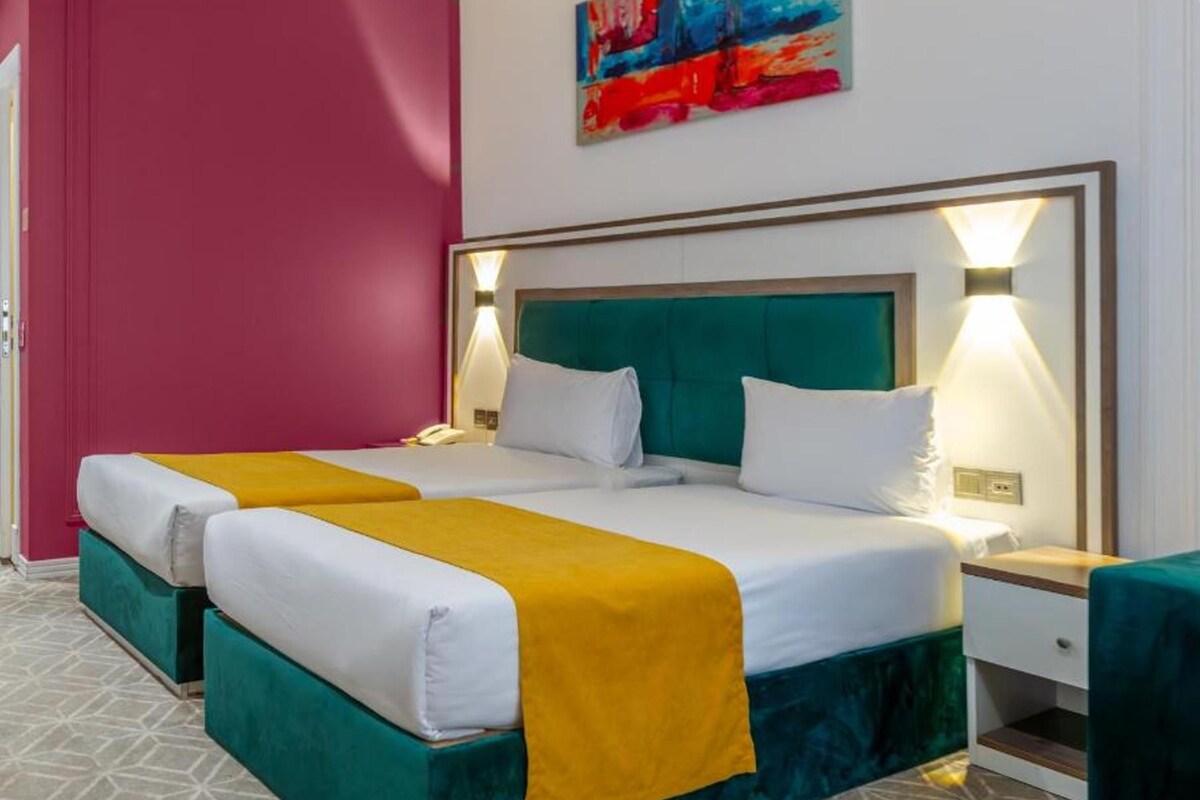 Ein Hotelzimmer mit einem Doppelbett, zwei Nachttischen, einem Wandbild und einem gemusterten Boden.