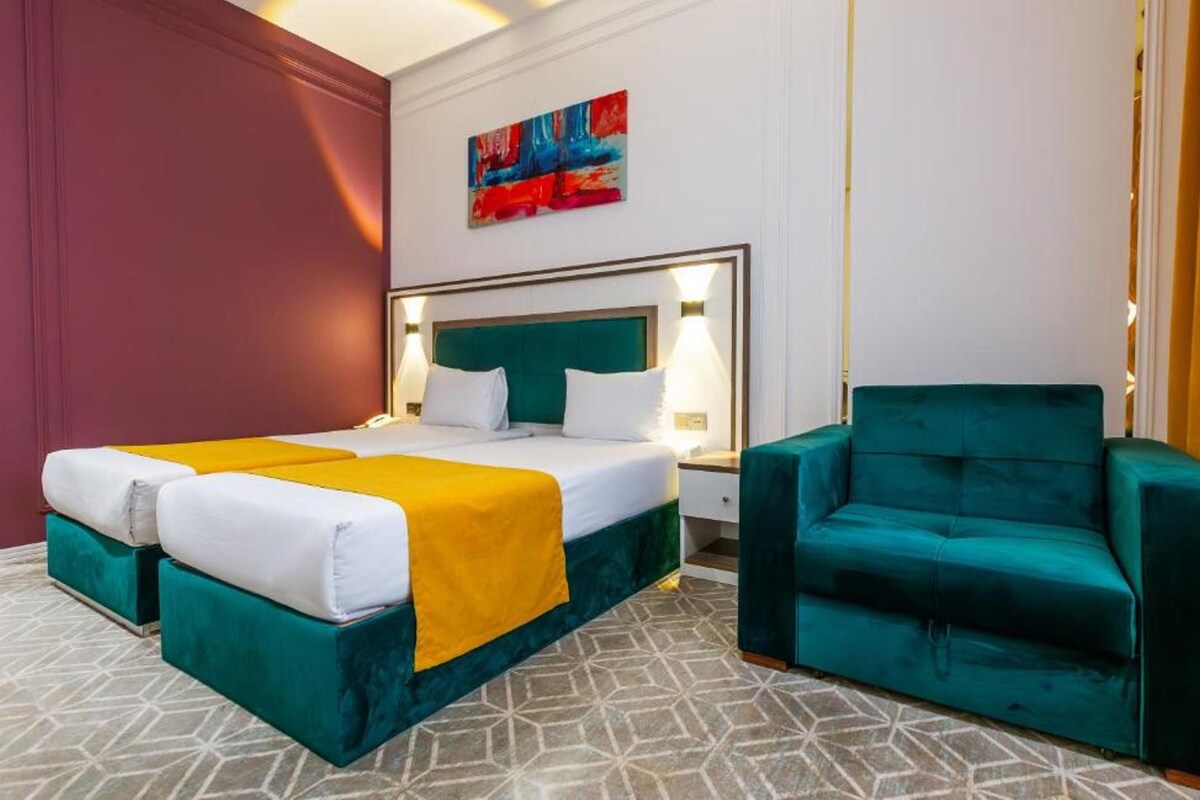 A hotel room with a bed, two bedside tables, a chair, a painting, and a patterned floor.