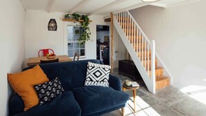 Un salón con un sofá azul oscuro, una escalera de madera y vistas a la cocina.
