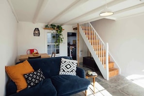 A living room with a dark blue sofa, a wooden staircase, and a view into the kitchen.
