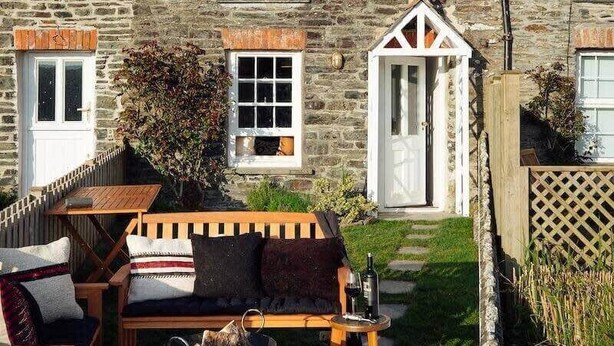 Una casa de piedra con un patio que cuenta con mobiliario exterior, una fogata y un pequeño jardín.
