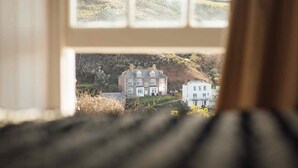 Vista a través de una ventana de una casa grande e histórica con fachada de piedra, múltiples chimeneas y un césped bien cuidado.