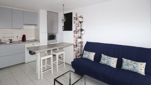 A compact living space with a kitchenette, a dining area, and a sofa with patterned cushions. - T2 Apartment with parking and garden 300 m from the beach (Banyuls-sur-Mer)
