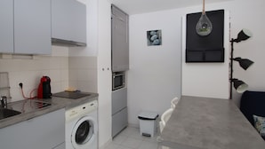 A compact kitchen with a washing machine, a microwave, and a small dining area with a table and chairs. - T2 Apartment with parking and garden 300 m from the beach (Banyuls-sur-Mer)