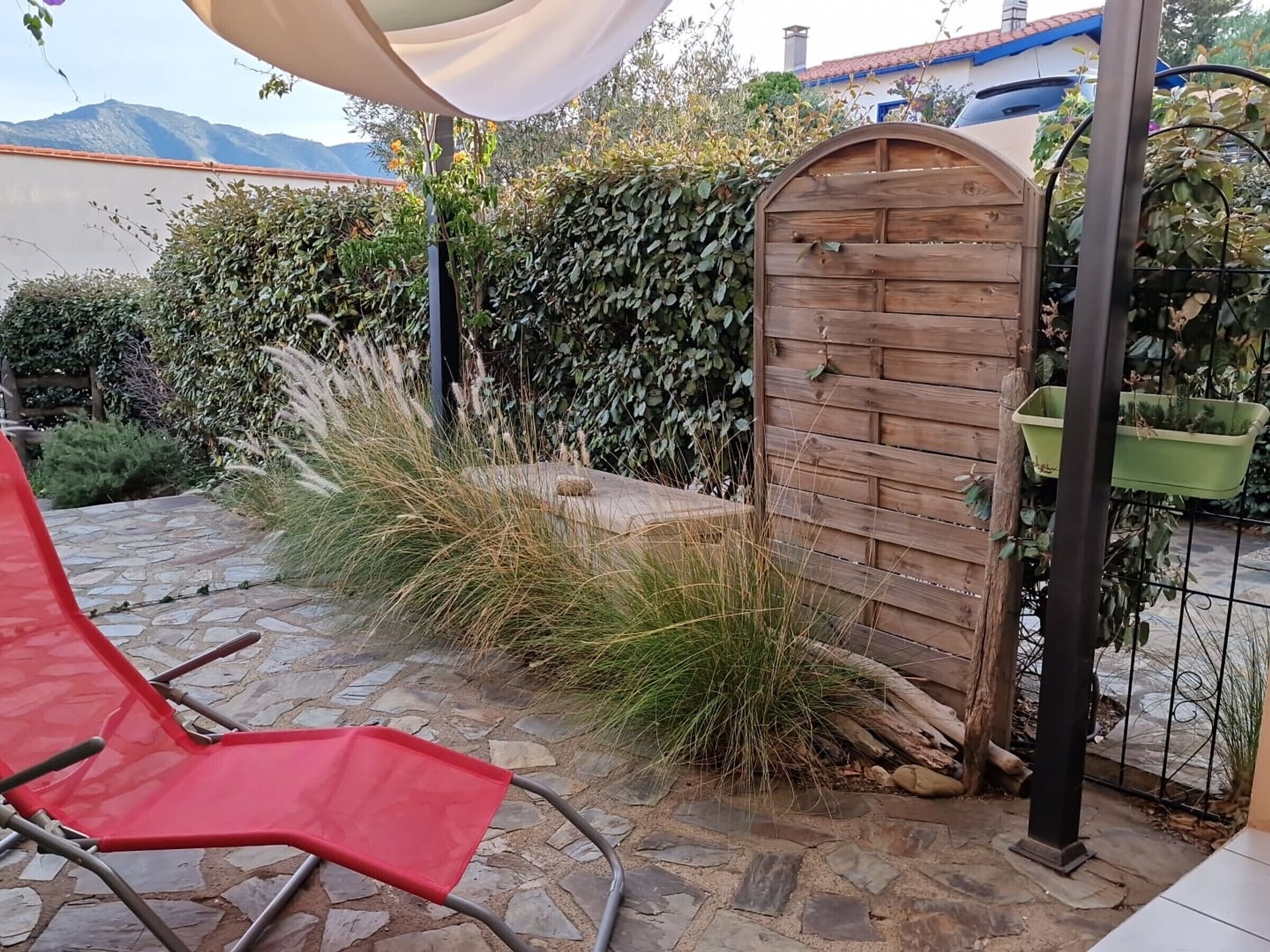 Een terras met een rode opklapstoel, een houten poort en een stenen pad.