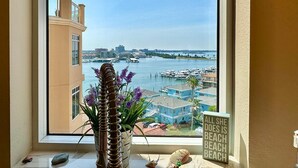 A view from a window overlooking a marina with boats, a city skyline, and a sign that reads "ALL SHE DOES IS BEACH BEACH BEACH".