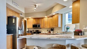 A modern kitchen with wooden cabinets, stainless steel appliances, a large island with stools, and a sign on the wall.