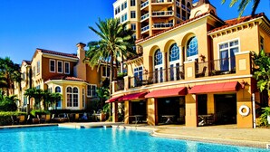 A hotel with a swimming pool, multiple balconies, and palm trees.