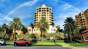 A multi-story hotel with a central courtyard, palm trees, and a visible rainbow.