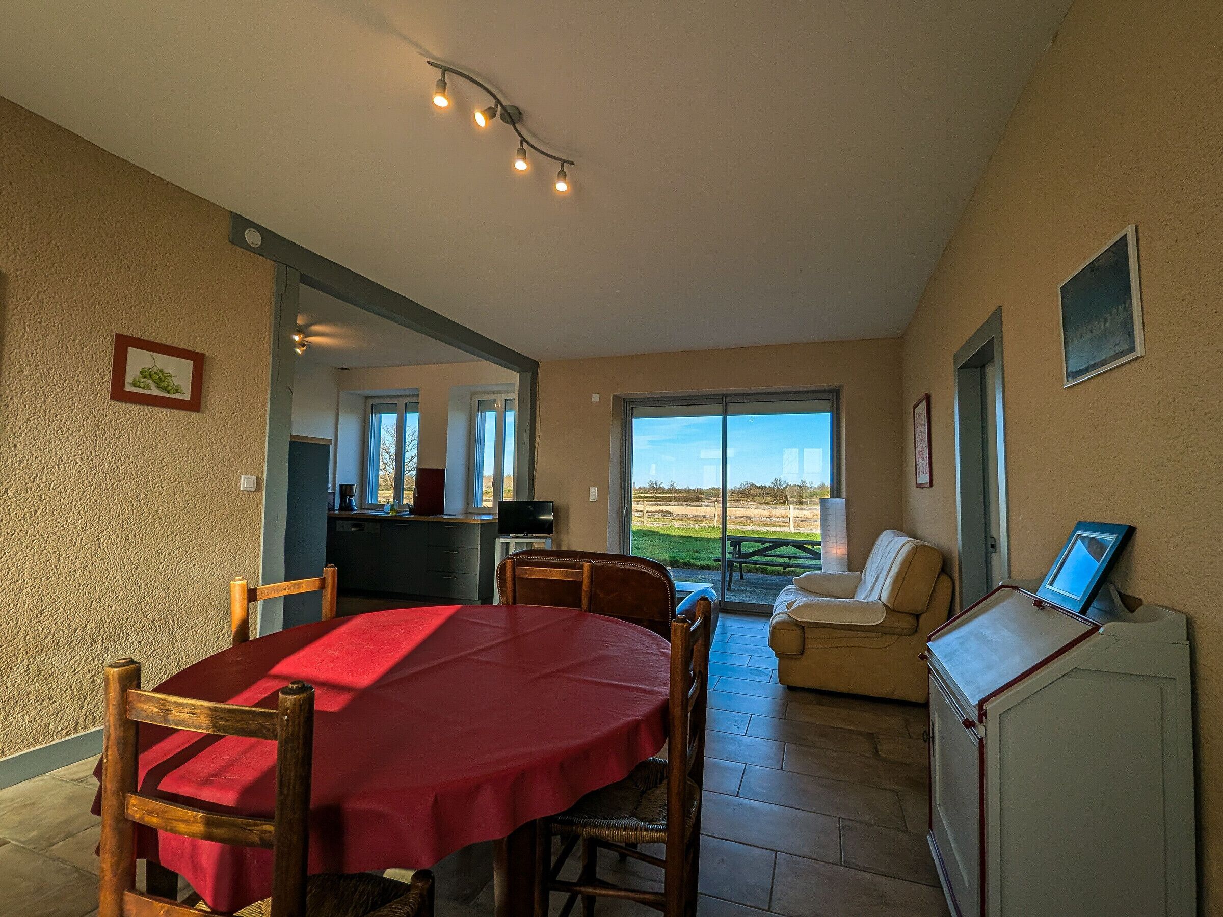 Un comedor con una mesa y sillas rojas, una cocina al fondo y vistas al exterior a través de amplios ventanales.