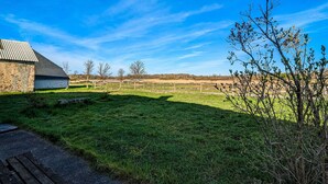 Un paysage rural avec un bâtiment en pierre, un champ verdoyant et un ciel bleu dégagé.