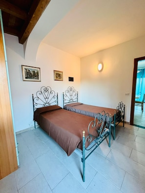 A room with two metal beds, a white wall, and a ceiling light. - Shardana 2 (San Teodoro)