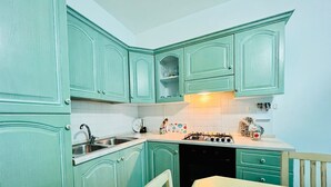 A kitchen with teal cabinets, a white countertop, a stove, and a sink. - Shardana 2 (San Teodoro)