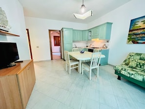 A compact living space with a dining area, kitchenette, and a television on a wooden cabinet. - Shardana 2 (San Teodoro)