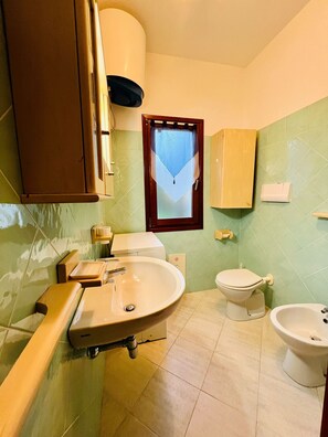 A bathroom with a sink, toilet, bidet, and a window with a curtain. - Shardana 2 (San Teodoro)