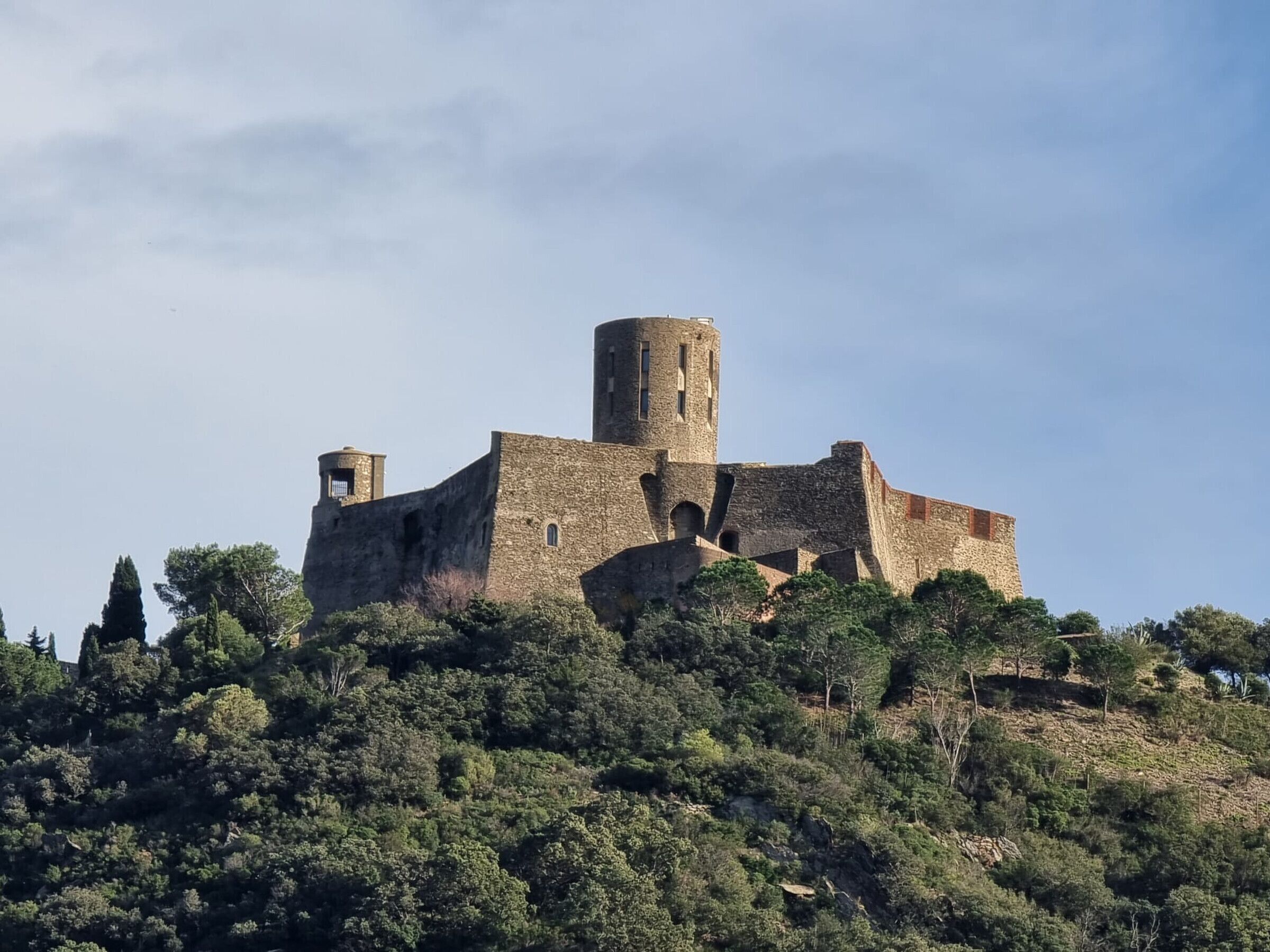Un château de pierre historique, perché sur une colline et entouré d’une végétation luxuriante.