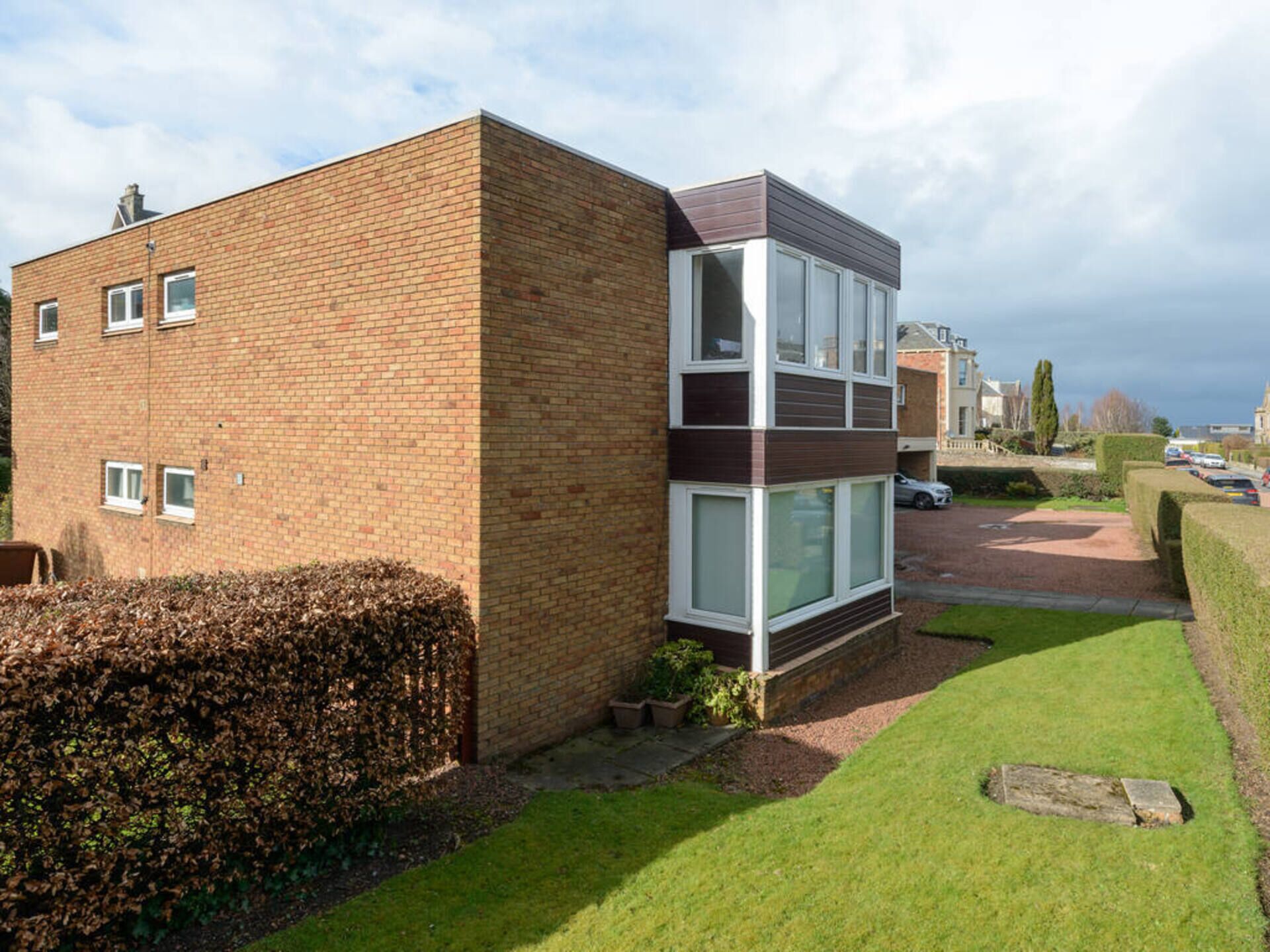 A modern two-story residential building with a brick facade, large windows, and a well-maintained lawn.