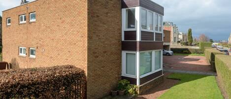 A modern two-story residential building with a brick facade, large windows, and a well-maintained lawn.