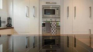 A modern kitchen with a built-in microwave, oven, and a reflective black countertop. - Corrin - Chic 1 Bedroom Apartment (North Berwick)