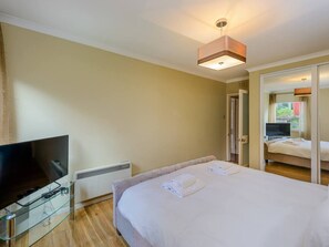 A hotel room with a large bed, a flat-screen TV on a glass table, and a ceiling light fixture. - Corrin - Chic 1 Bedroom Apartment (North Berwick)