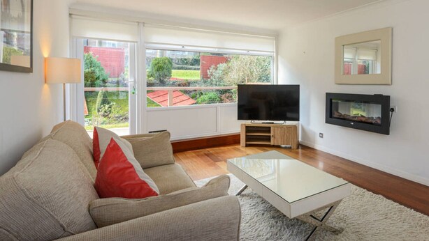 A living room with a sofa, a glass coffee table, a flat-screen TV on a wooden stand, and a fireplace. - Corrin - Chic 1 Bedroom Apartment (North Berwick)