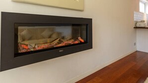 A modern fireplace with a glass front, set in a white wall with a wooden floor. - Corrin - Chic 1 Bedroom Apartment (North Berwick)