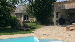 Una piscina con lettini, un edificio in pietra e un'area barbecue.