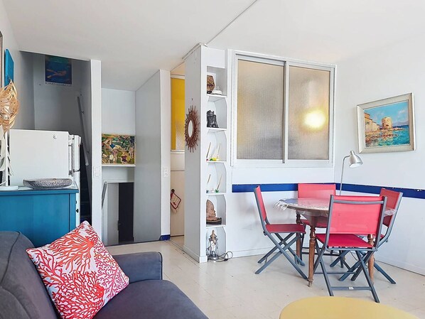 A compact living space with a kitchenette, a dining area with red chairs, and a sofa with a red and white patterned pillow.