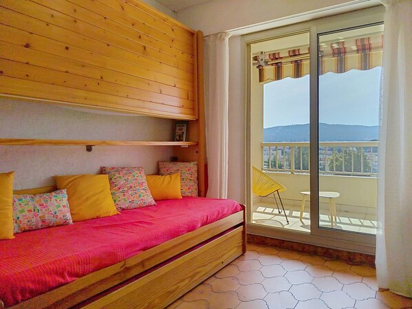 Una habitación con cama, ventana con vistas y balcón con una silla.