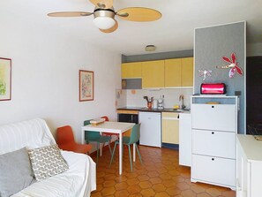 Un espacio habitable compacto con kitchenette, una zona de comedor con sillas, una cama con almohadas y un ventilador de techo.
