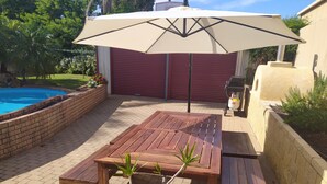 Eine Holzterrasse mit Tisch und Bänken, ein Schwimmbad und eine rote Garagentür.
