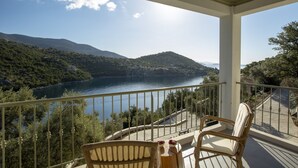 Varanda com cadeiras de vime e uma mesa, com vista para um lago e colinas.